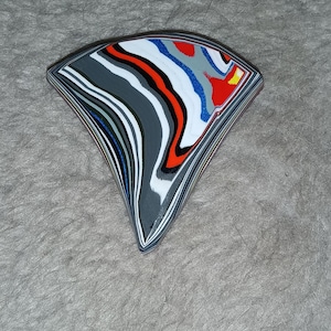 May include: A colorful, layered agate stone with a fan shape. The stone has a variety of colors, including red, orange, yellow, blue, white, and gray.
