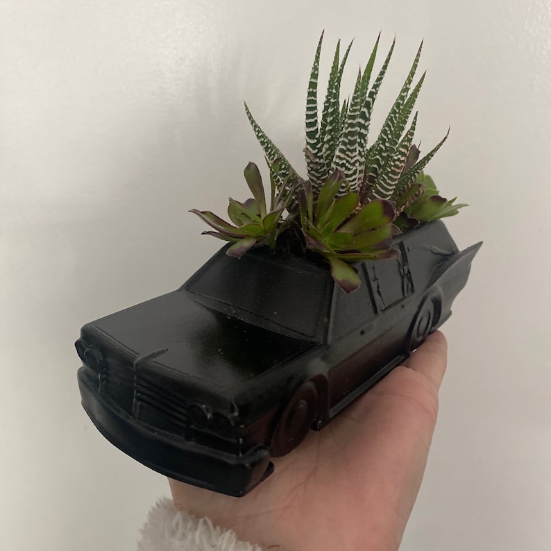 May include: A black ceramic planter shaped like a vintage car, with a variety of succulents growing inside.