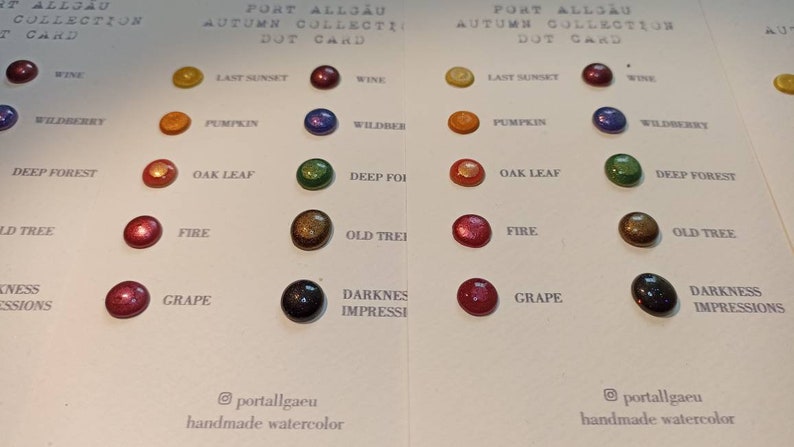 Peut inclure: Une carte de points de la collection d'automne Port Allg&auml;u, pr&eacute;sentant des points d'aquarelle de diff&eacute;rentes couleurs. Chaque point est &eacute;tiquet&eacute; avec un nom de couleur, comme "Wine", "Last Sunset" et "Wildberry". La carte comprend le texte "handmade watercolor".