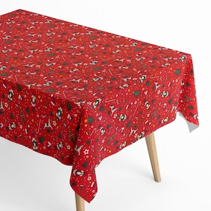 Op de afbeelding: Een rode rechthoekige tafelkleed met een feestelijk kerstpatroon. Het ontwerp omvat witte sterren, groene kerstbomen, rendieren, notenkrakers en zuurstokken. Het tafelkleed wordt gepresenteerd op een houten tafel.