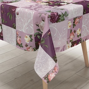 Puede incluir: Un mantel rosa y morado con un patrón floral que presenta rosas y espirales. El mantel está hecho de vinilo y tiene una textura acolchada.
