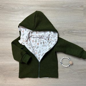 Op de afbeelding: Een donkergroen hooded jack met een witte en bruine geprinte voering. Het jack heeft een ritssluiting en is gemaakt van een zachte, warme stof.