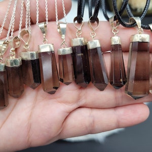 May include: A collection of ten smoky quartz crystal pendants on silver and black chains. The crystals are faceted and have a pointed shape.