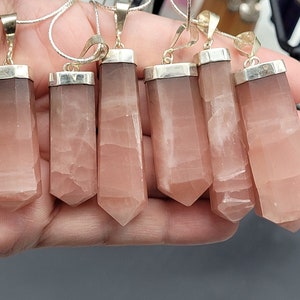 May include: Seven pink crystal pendants with silver settings. The pendants are all in the shape of a long, thin point. They are hanging from silver chains.