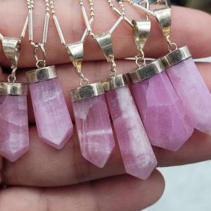 May include: Seven pink crystal pendants with silver settings on silver chains. The crystals are all different sizes and shapes, but they are all cut into a point at the bottom.