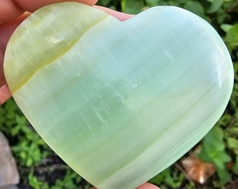 May include: A heart-shaped green and white polished stone with a smooth, polished surface.
