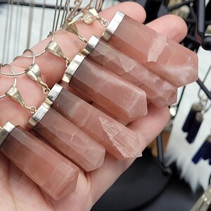 May include: Six pink and brown crystal pendants with silver bails on silver chains. The pendants are all different shapes and sizes, but they are all roughly rectangular. The crystals are translucent and have a slight shimmer to them.