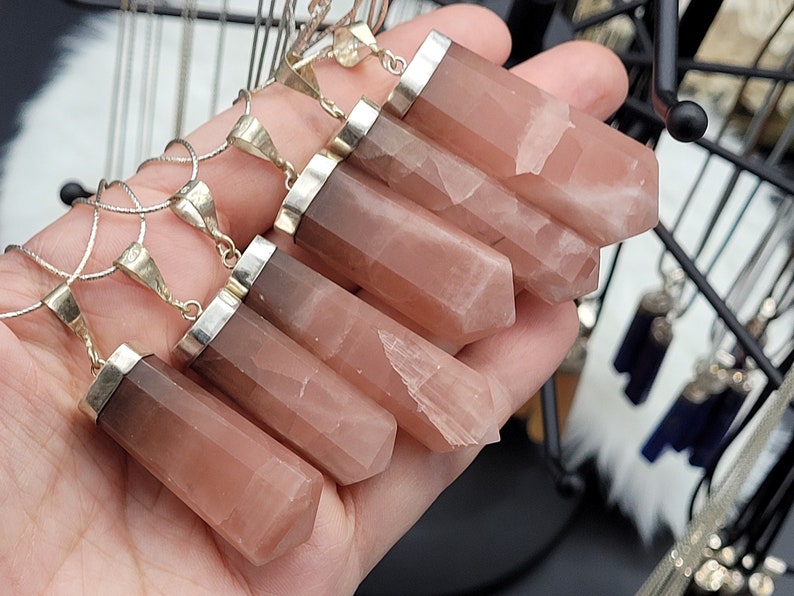May include: Six pink and brown crystal pendants with silver bails on silver chains. The pendants are all different shapes and sizes, but they are all roughly rectangular. The crystals are translucent and have a slight shimmer to them.