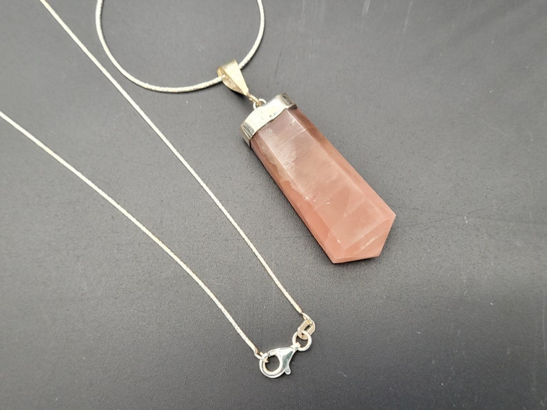 May include: A silver chain necklace with a pink crystal pendant. The pendant is a long, rectangular shape with a pointed end.