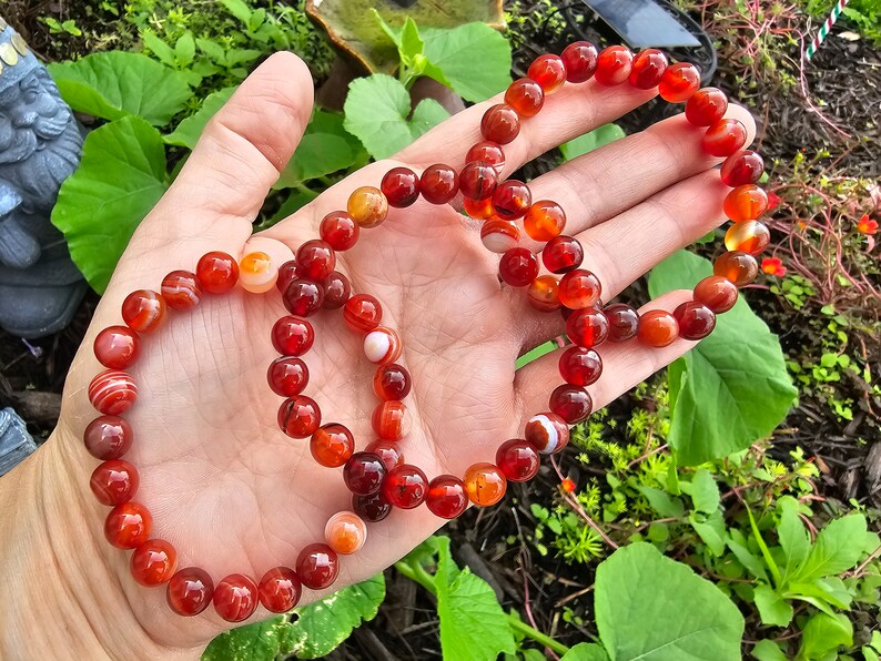 May include: Three red carnelian bracelets with white stripes. The bracelets are made of round beads and are stacked on top of each other.
