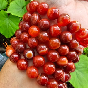 May include: A bracelet made of carnelian beads. The beads are a deep orange color with white stripes. The bracelet is on a person's wrist.
