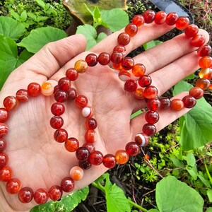 May include: Three red carnelian bracelets with white stripes. The bracelets are made of round beads and are stacked on top of each other.