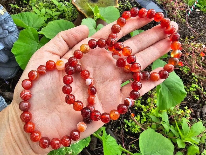 May include: Three red carnelian bracelets with white stripes. The bracelets are made of round beads and are stacked on top of each other.