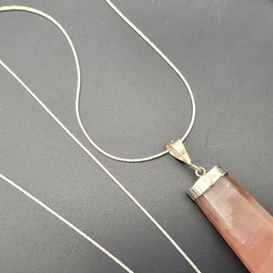 May include: A silver chain necklace with a pink crystal pendant. The pendant is a long, rectangular shape with a silver setting.