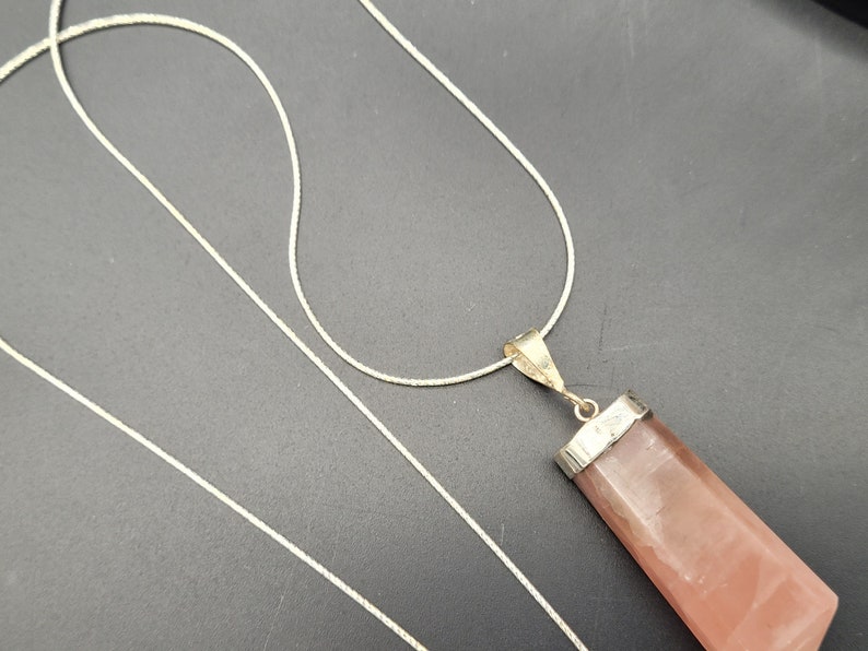 May include: A silver chain necklace with a pink crystal pendant. The pendant is a long, rectangular shape with a silver setting.