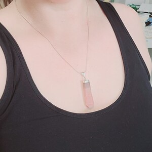 May include: A silver chain necklace with a pink and grey crystal pendant. The pendant is shaped like a long, thin rectangle with pointed ends.