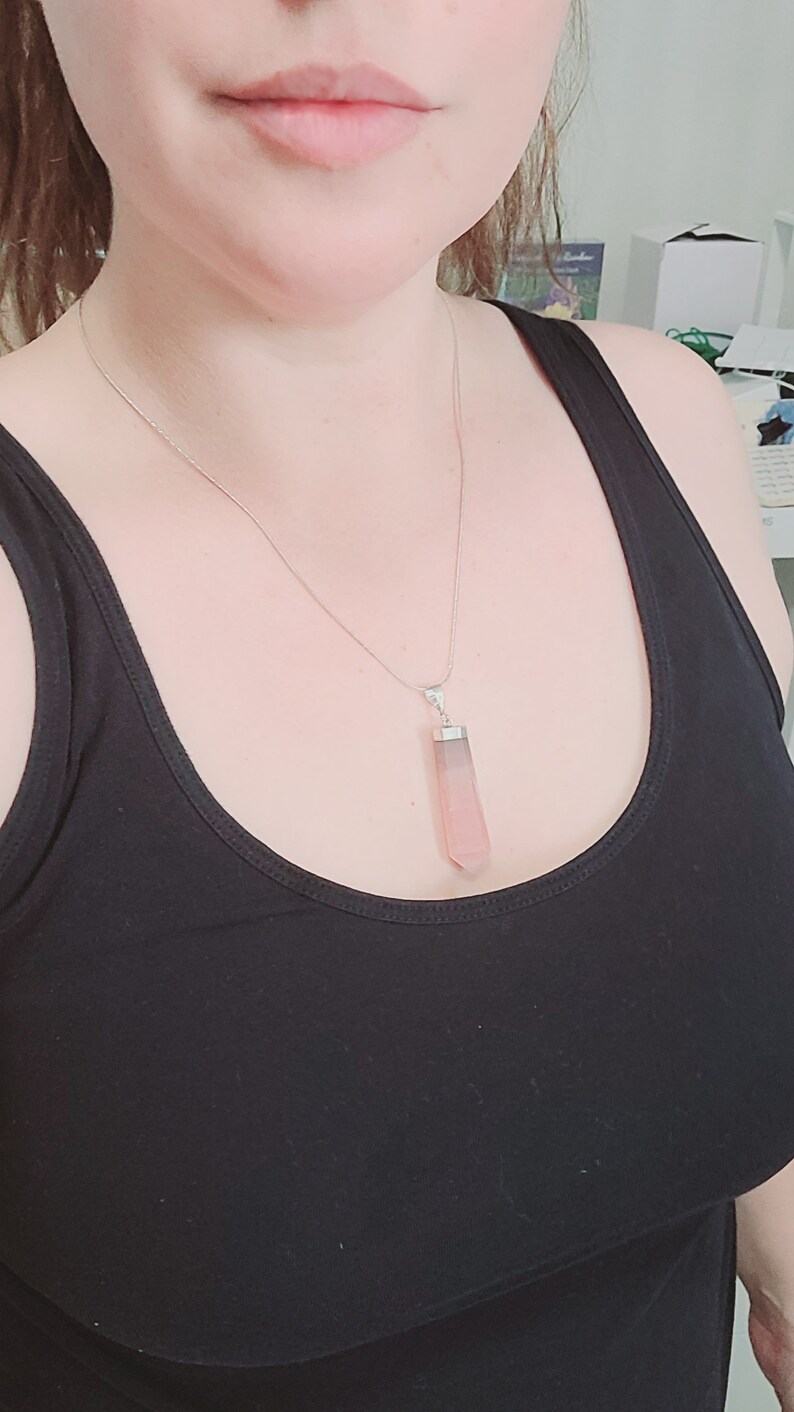 May include: A silver chain necklace with a pink and grey crystal pendant. The pendant is shaped like a long, thin rectangle with pointed ends.