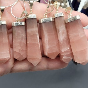 May include: Seven silver pendants with pink crystal stones. The stones are faceted and have a pointed shape. The pendants are all hanging from silver chains.