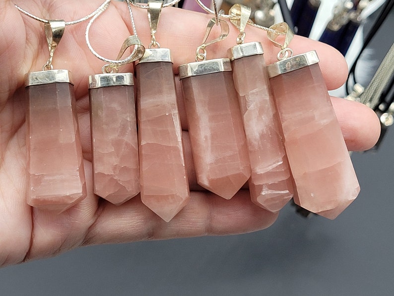 May include: Seven silver pendants with pink crystal stones. The stones are faceted and have a pointed shape. The pendants are all hanging from silver chains.