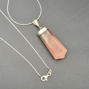 May include: A silver chain necklace with a pink crystal pendant. The pendant is a long, pointed shape with a silver setting.
