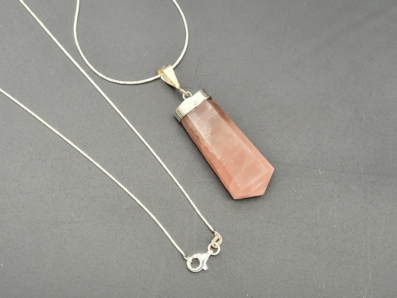 May include: A silver chain necklace with a pink crystal pendant. The pendant is a long, pointed shape with a silver setting.