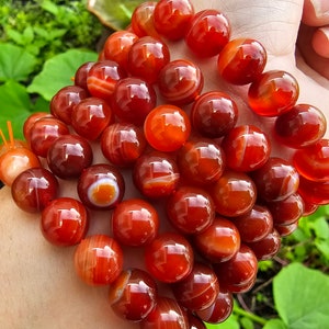 May include: A strand of carnelian beads, featuring a mix of red and orange tones with white banding. The beads are round and smooth, with a polished finish.