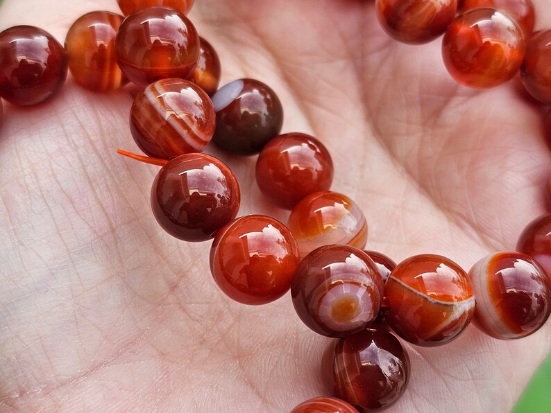 May include: A strand of carnelian beads, featuring a mix of red and white banded agate stones. The beads are round and polished, with a glossy finish.