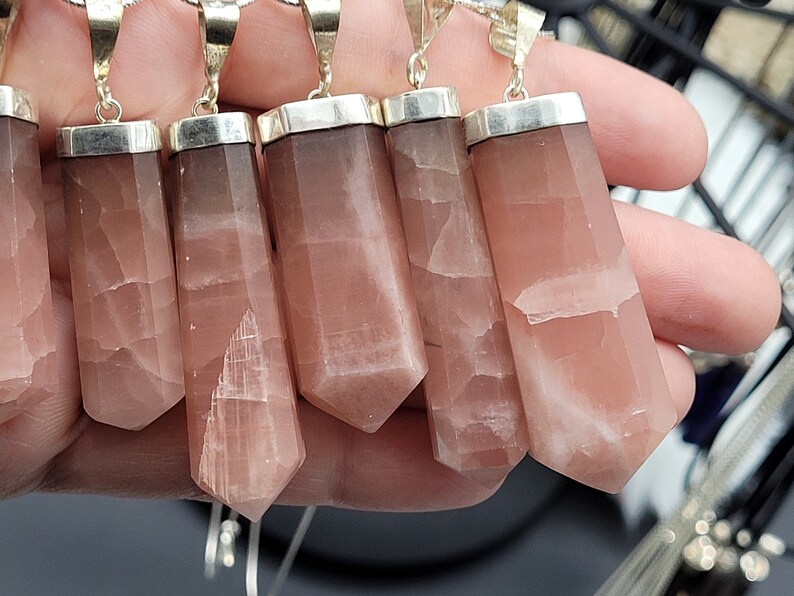 May include: Six pink and white gemstone pendants with silver settings. The pendants are in the shape of a long, thin rectangle with a pointed end.