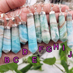 May include: A collection of gemstone pendants with silver-colored metal caps and bails. The pendants are elongated, with a pointed bottom and a variety of colors, including blue, green, and white. Each pendant is approximately 2-3 inches long.
