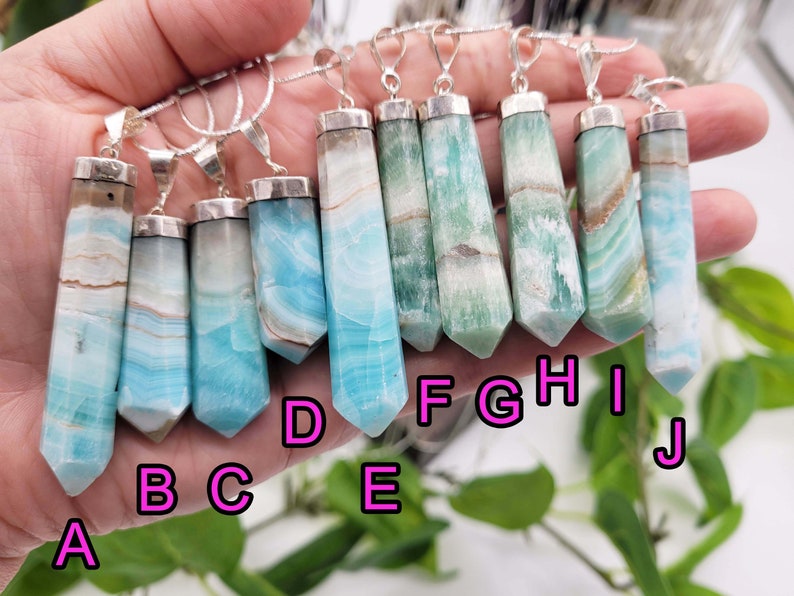 May include: A collection of gemstone pendants with silver-colored metal caps and bails. The pendants are elongated, with a pointed bottom and a variety of colors, including blue, green, and white. Each pendant is approximately 2-3 inches long.