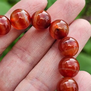 May include: A close-up of a red carnelian bracelet with round beads. The beads are polished and have a natural, striated pattern.