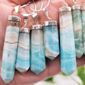 May include: A collection of gemstone pendants with silver-colored metal caps and bails. The pendants are rectangular with a pointed bottom and feature bands of blue, white, and brown colors. Some pendants are green.