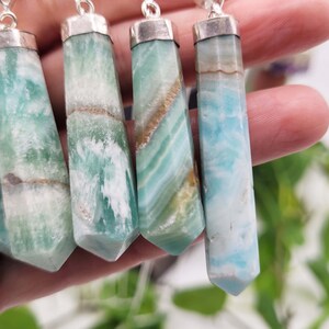 May include: A collection of gemstone pendants with silver-colored caps and chains. The pendants are hexagonal, with a variety of colors including light blue, green, and brown. The gemstones have a polished, smooth surface.