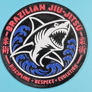 May include: A circular patch featuring a white shark with an open mouth, surrounded by blue waves on a black background. The border contains the red text BRAZILIAN JIU-JITSU, DISCIPLINE, RESPECT, EVOLUTION, and Japanese characters.