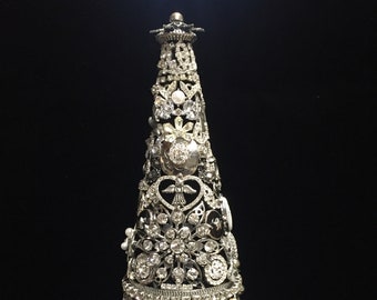 May include: A silver and crystal Christmas tree ornament, decorated with rhinestones, buttons, and other embellishments.