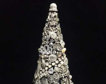 May include: A decorative Christmas tree made of silver-toned embellishments. The tree is cone-shaped and covered in various charms, including stars, hearts, and floral designs. The tree is set against a black background.