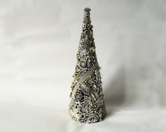 May include: A silver cone-shaped Christmas tree covered in rhinestones, jewels, and other decorative embellishments.