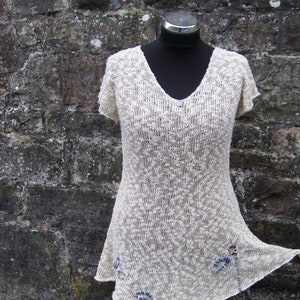 May include: A white crocheted top with a loose, flowing fit and a V-neckline. The top features delicate blue and red embroidery details.