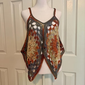 May include: A crocheted top with a geometric pattern in shades of brown, beige, and gray. The top has a V-neck and thin straps.
