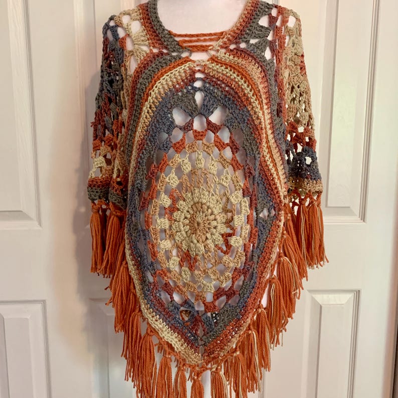 May include: A crocheted poncho with a multi-colored circular design and orange fringe.