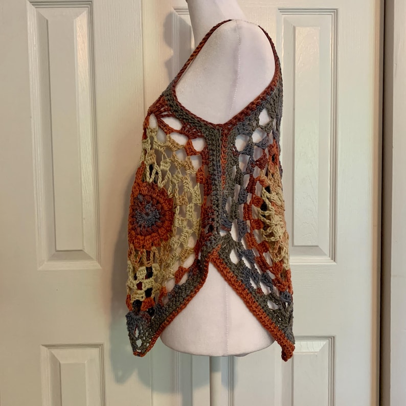 May include: A crocheted top with a geometric pattern in shades of orange, brown, beige, and gray. The top has a loose, flowy fit and a slightly asymmetrical hemline.