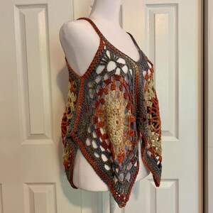May include: A crocheted top with a geometric pattern in shades of brown, orange, and gray. The top has a loose, flowing fit and a triangular shape.