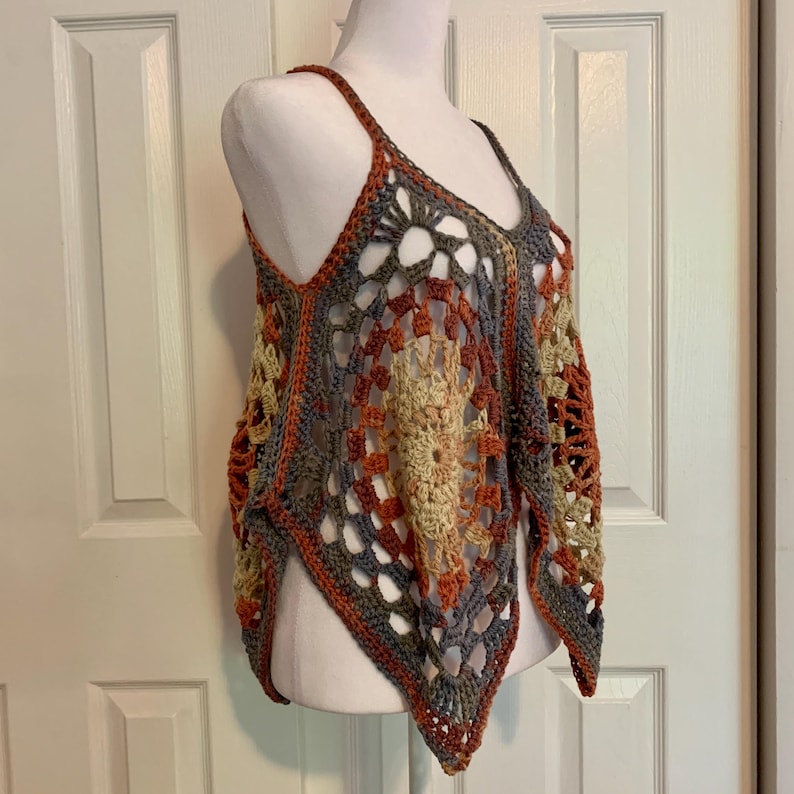 May include: A crocheted top with a geometric pattern in shades of brown, orange, and gray. The top has a loose, flowing fit and a triangular shape.