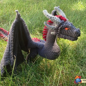 Peut inclure: Un jouet de dragon en crochet fait de fil gris et rouge. Le dragon a une longue queue, des ailes et une t&ecirc;te avec des yeux orange.