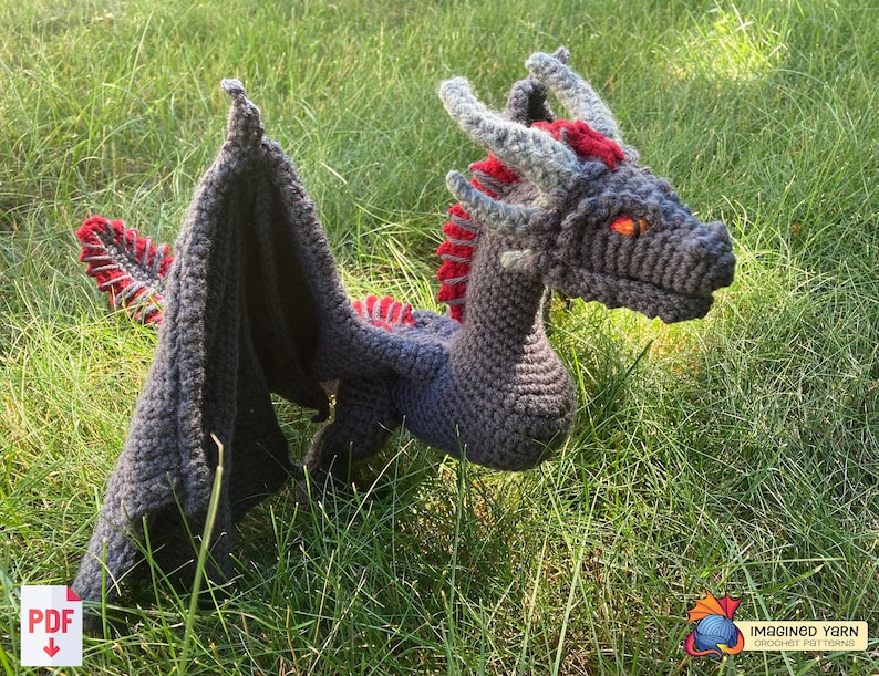 Peut inclure: Un jouet de dragon en crochet fait de fil gris et rouge. Le dragon a une longue queue, des ailes et une t&ecirc;te avec des yeux orange.