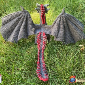 Peut inclure: Un jouet de dragon en crochet avec des ailes grises et une queue rouge et grise. Le dragon est couch&eacute; sur le dos, les ailes d&eacute;ploy&eacute;es.