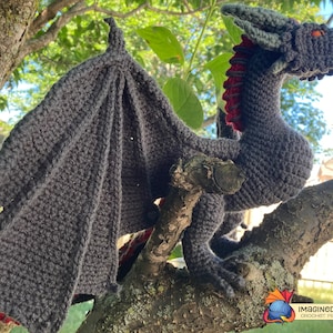 Peut inclure: Un dragon gris en crochet avec des accents rouges perch&eacute; sur une branche d'arbre. Le dragon a une longue queue et de grandes ailes. Le mod&egrave;le de crochet est disponible en t&eacute;l&eacute;chargement PDF.