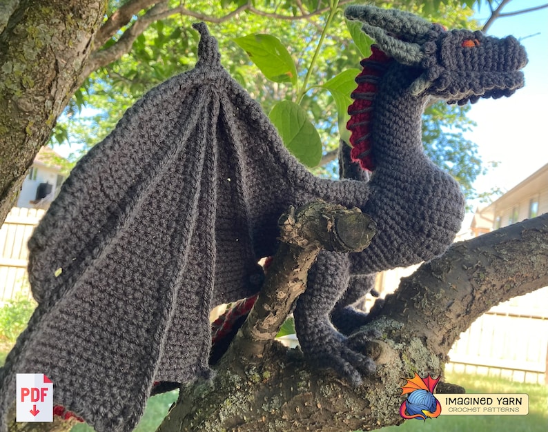 Peut inclure: Un dragon gris en crochet avec des accents rouges perch&eacute; sur une branche d'arbre. Le dragon a une longue queue et de grandes ailes. Le mod&egrave;le de crochet est disponible en t&eacute;l&eacute;chargement PDF.