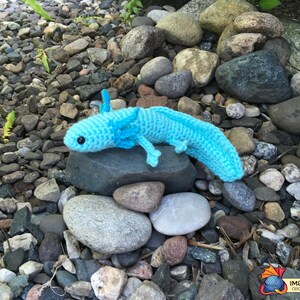 May include: A crocheted blue axolotl, a type of salamander, is sitting on a rock. The axolotl is a popular pet and is known for its unique appearance.