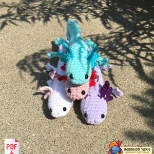May include: Four crocheted axolotl plushies stacked on top of each other. The top axolotl is turquoise, the next is pink, the next is white, and the bottom axolotl is purple. The axolotls are all facing the camera.